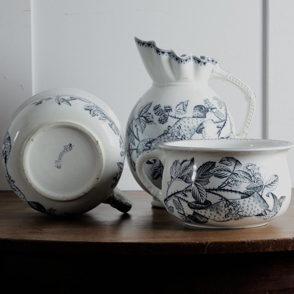 An early 20th-century white ceramic wash set featuring a large ewer and two chamber pots decorated with a black botanical blackberry transferware pattern. View II