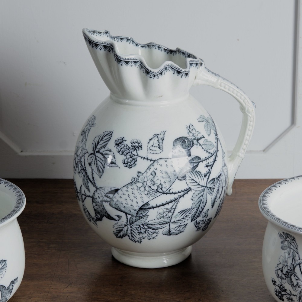 An early 20th-century white ceramic wash set featuring a large ewer and two chamber pots decorated with a black botanical blackberry transferware pattern. View XIV