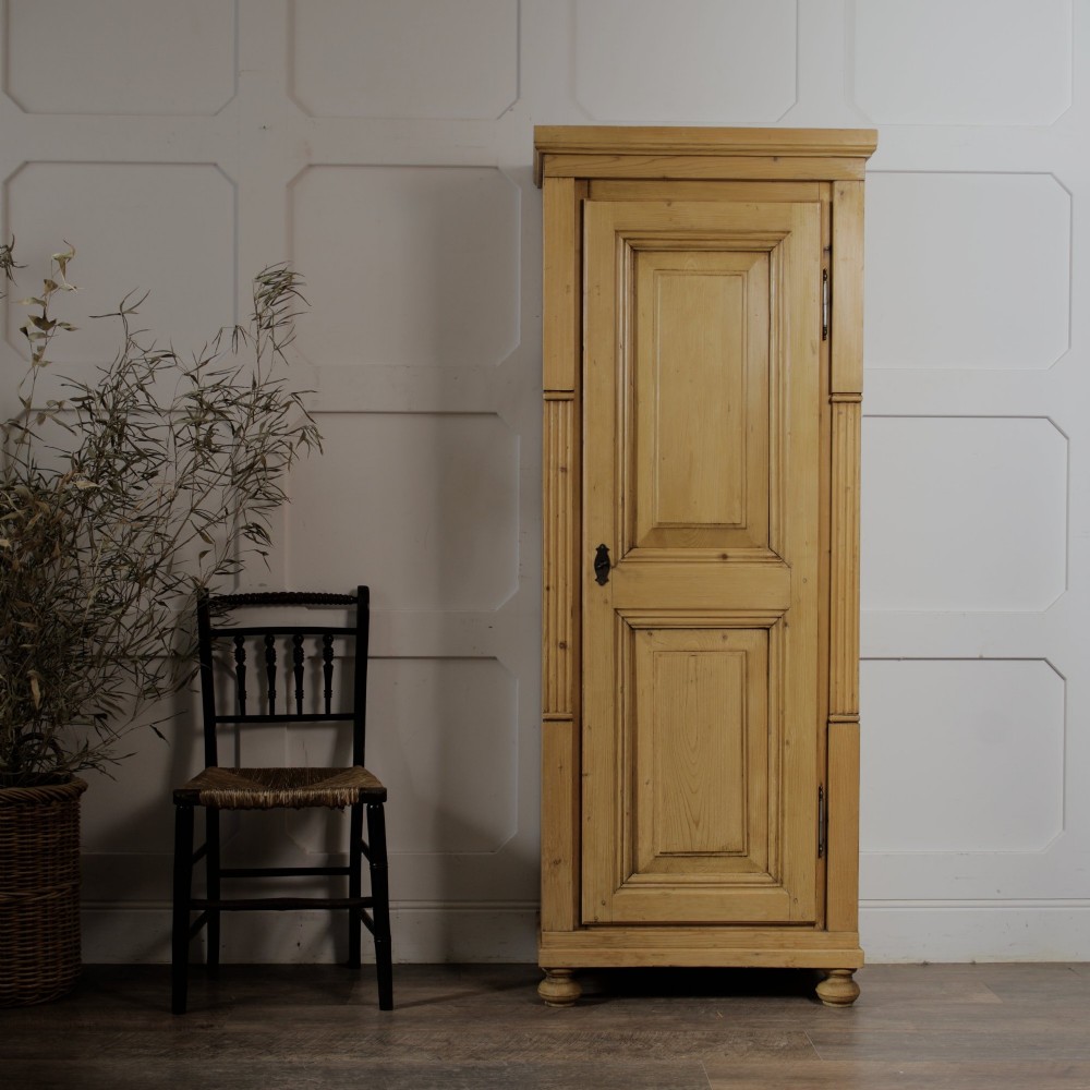 A tall single door stripped pine armoire featuring fielded panels, fluted side pilasters, and turned bun feet. View II