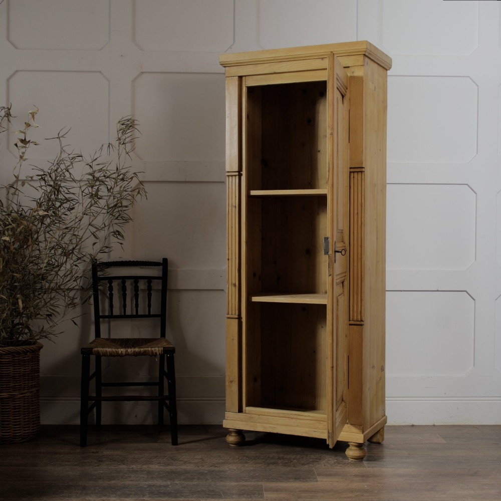 A tall single door stripped pine armoire featuring fielded panels, fluted side pilasters, and turned bun feet. View III