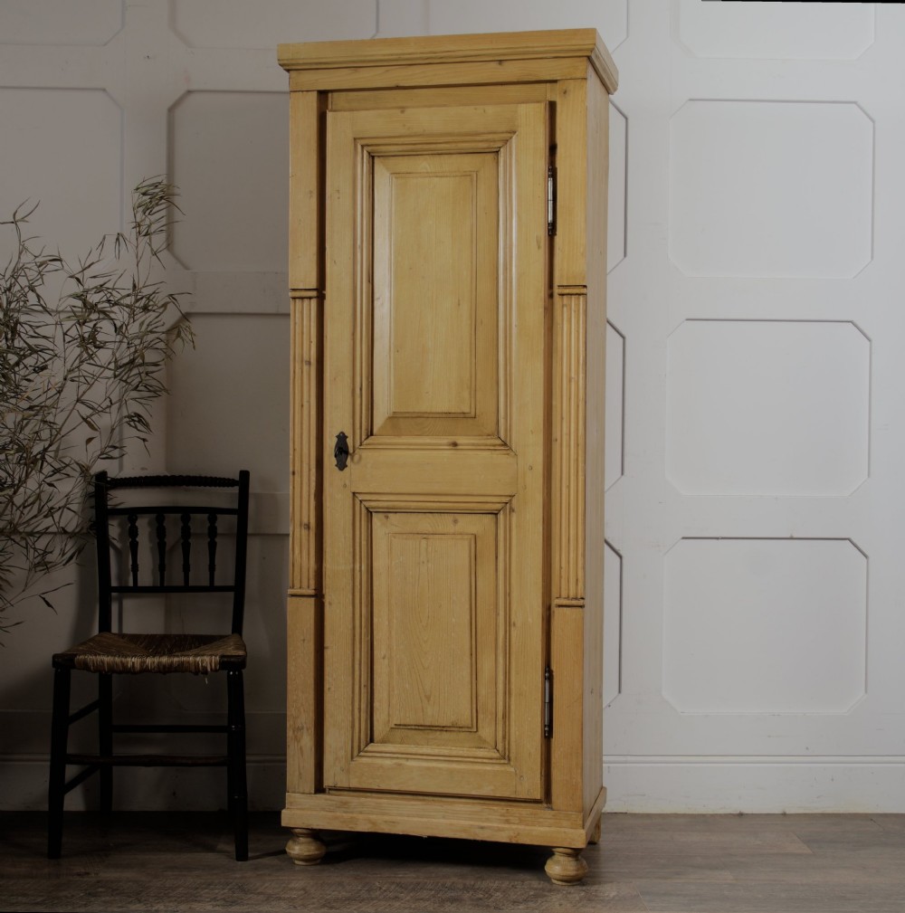 A tall single door stripped pine armoire featuring fielded panels, fluted side pilasters, and turned bun feet. View IV