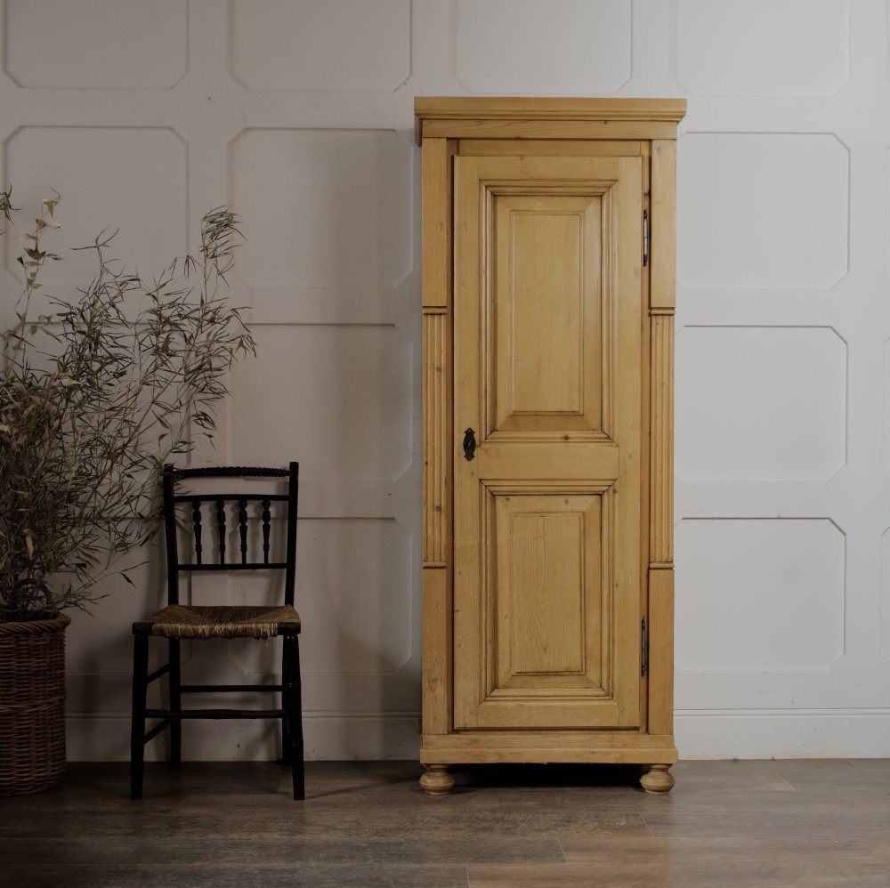 A tall single door stripped pine armoire featuring fielded panels, fluted side pilasters, and turned bun feet. View V