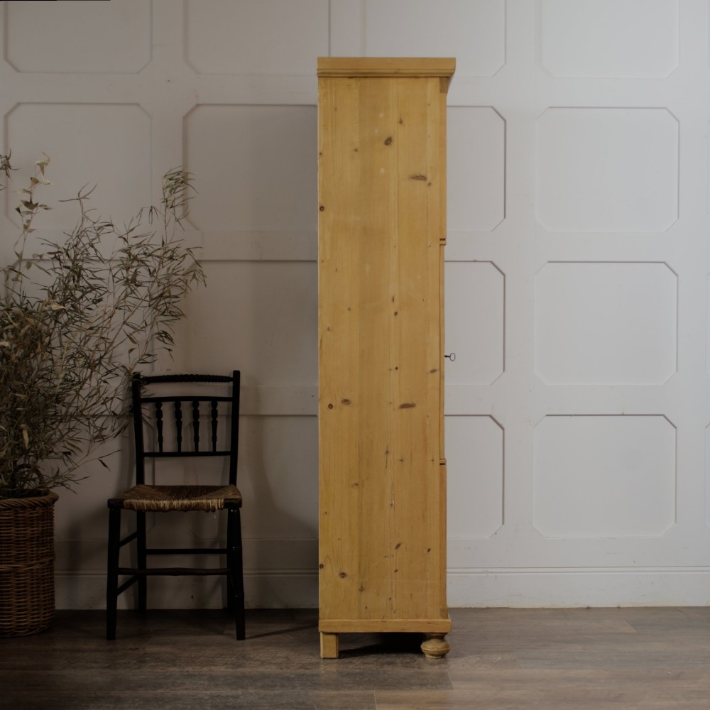 A tall single door stripped pine armoire featuring fielded panels, fluted side pilasters, and turned bun feet. View VI
