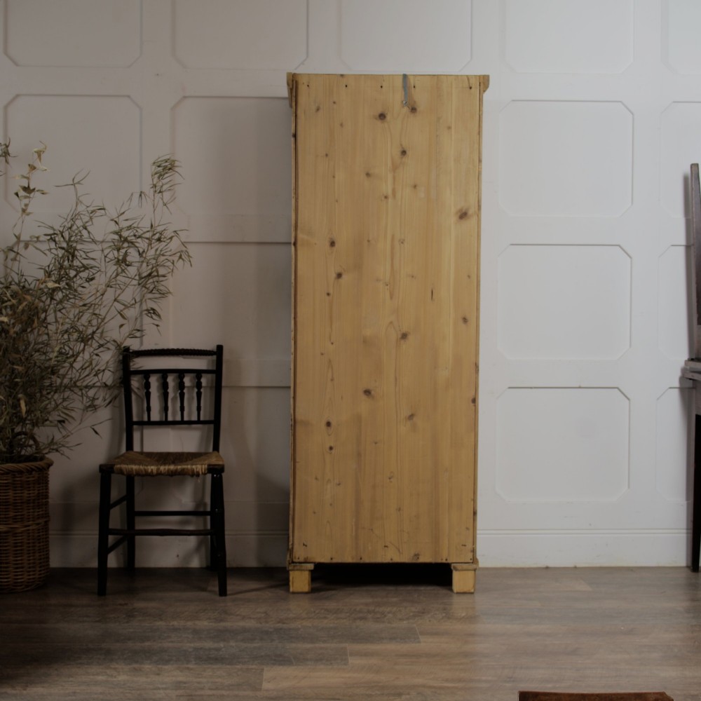 A tall single door stripped pine armoire featuring fielded panels, fluted side pilasters, and turned bun feet. View VII