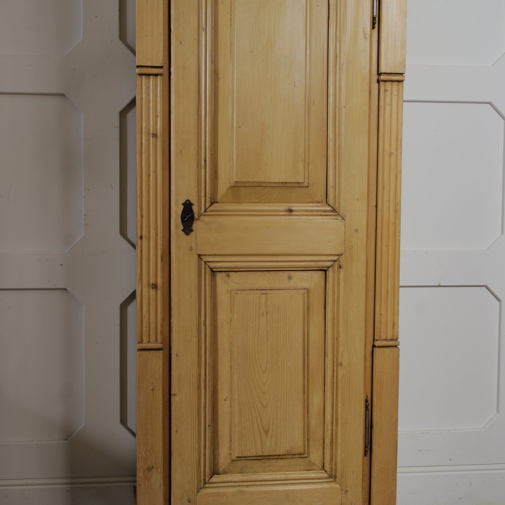 A tall single door stripped pine armoire featuring fielded panels, fluted side pilasters, and turned bun feet. View VIII