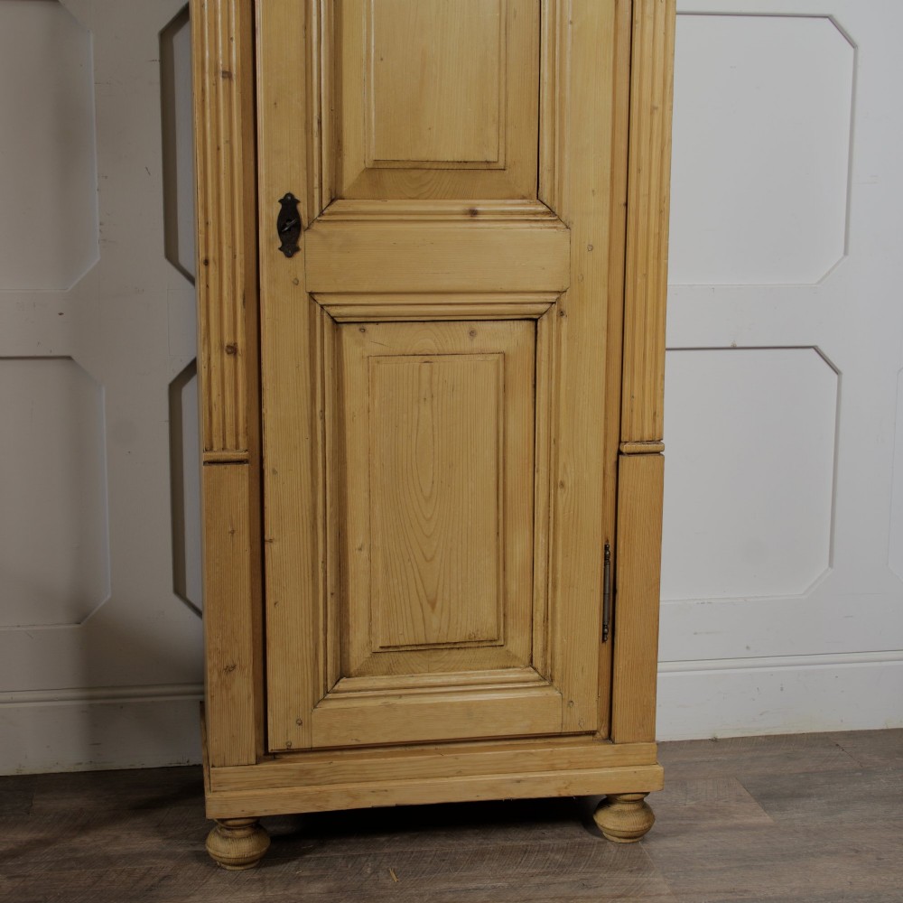A tall single door stripped pine armoire featuring fielded panels, fluted side pilasters, and turned bun feet. View IX