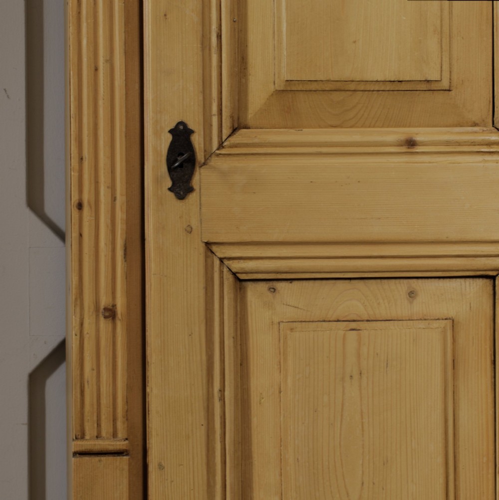 A tall single door stripped pine armoire featuring fielded panels, fluted side pilasters, and turned bun feet. View X