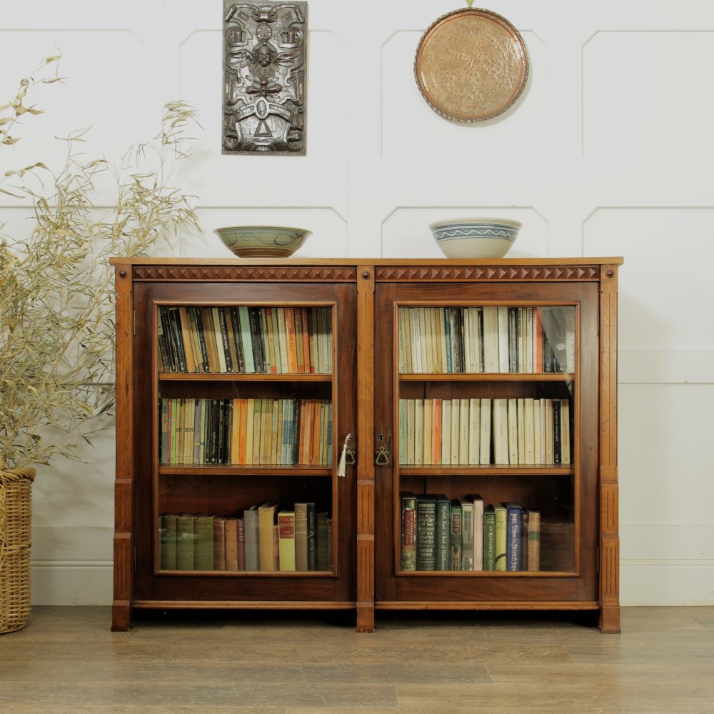 An early 20th-century low double-section wooden bookcase featuring glazed doors with carved diamond border trim and three internal shelf levels filled with books.