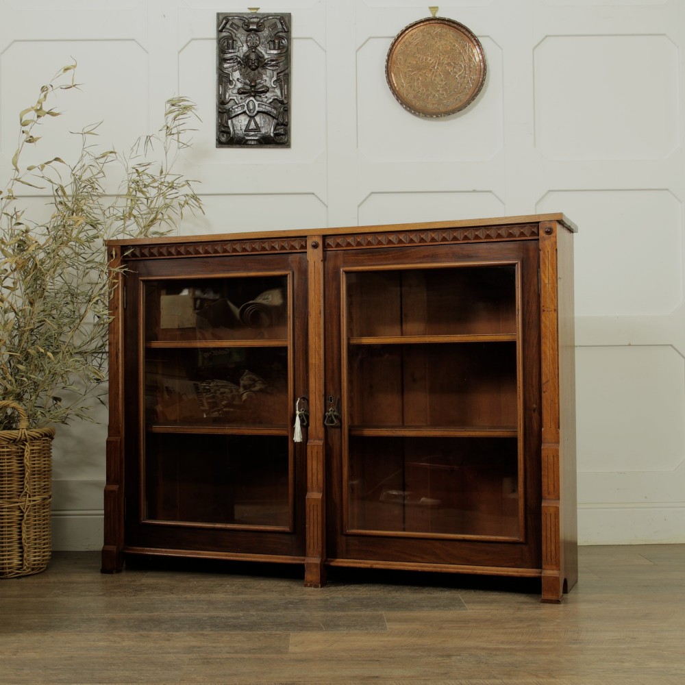 An early 20th-century low double-section wooden bookcase featuring glazed doors with carved diamond border trim and three internal shelf levels filled with books. View II