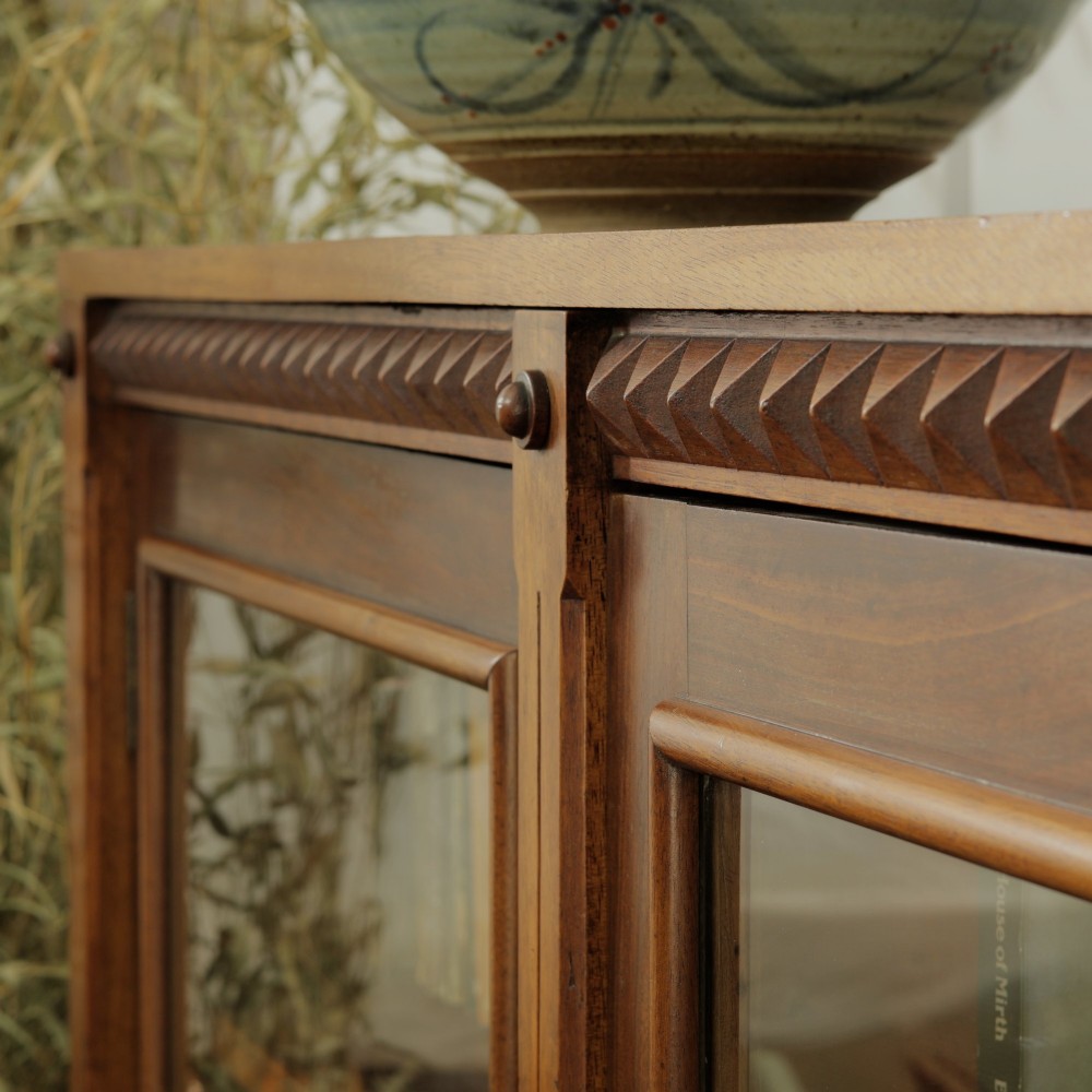 An early 20th-century low double-section wooden bookcase featuring glazed doors with carved diamond border trim and three internal shelf levels filled with books. View III