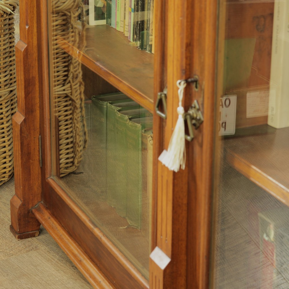 An early 20th-century low double-section wooden bookcase featuring glazed doors with carved diamond border trim and three internal shelf levels filled with books. View IV