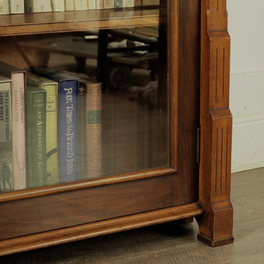 An early 20th-century low double-section wooden bookcase featuring glazed doors with carved diamond border trim and three internal shelf levels filled with books. View V