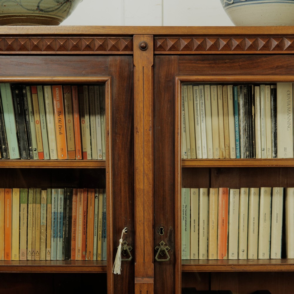 An early 20th-century low double-section wooden bookcase featuring glazed doors with carved diamond border trim and three internal shelf levels filled with books. View VI