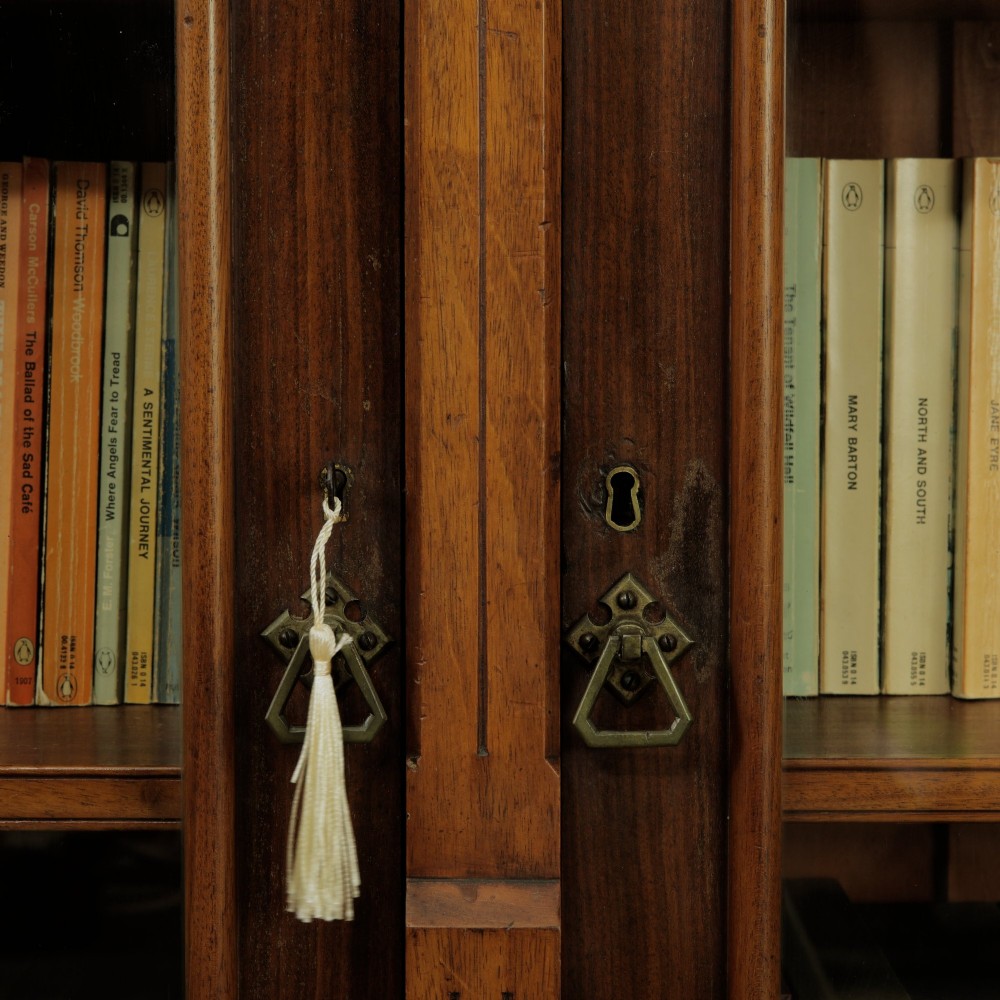 An early 20th-century low double-section wooden bookcase featuring glazed doors with carved diamond border trim and three internal shelf levels filled with books. View VII