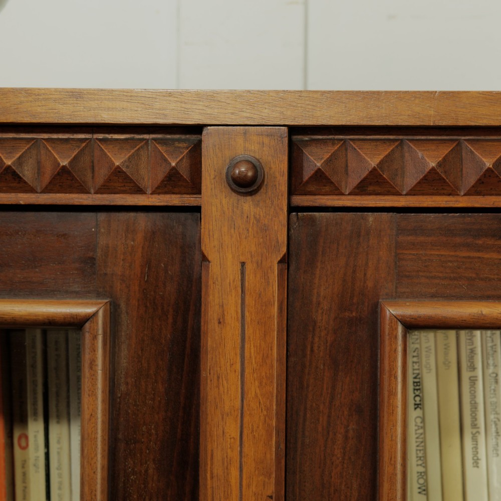 An early 20th-century low double-section wooden bookcase featuring glazed doors with carved diamond border trim and three internal shelf levels filled with books. View VIII