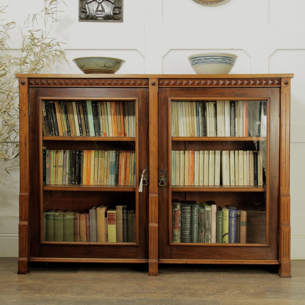 An early 20th-century low double-section wooden bookcase featuring glazed doors with carved diamond border trim and three internal shelf levels filled with books. View IX