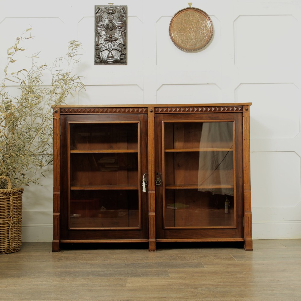 An early 20th-century low double-section wooden bookcase featuring glazed doors with carved diamond border trim and three internal shelf levels filled with books. View X