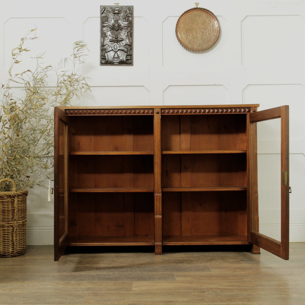 An early 20th-century low double-section wooden bookcase featuring glazed doors with carved diamond border trim and three internal shelf levels filled with books. View XI