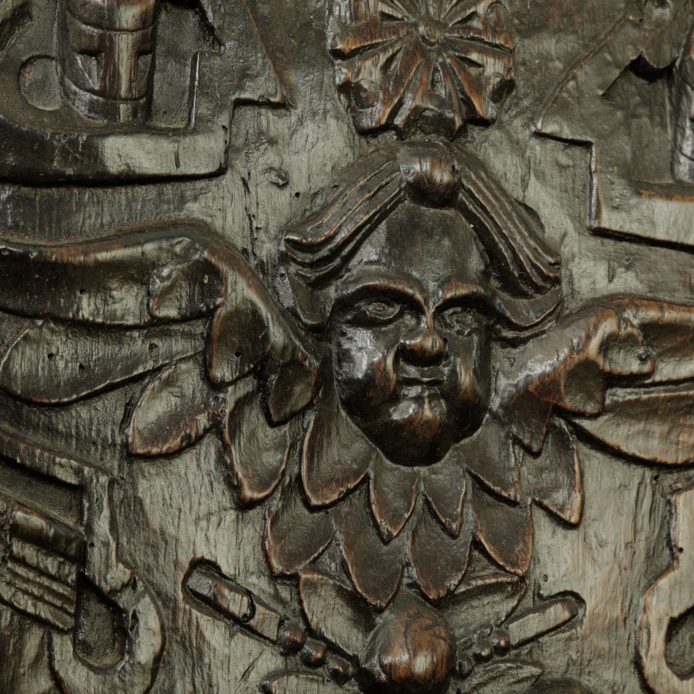 A rectangular dark oak timber panel featuring a high-relief hand carving of a winged cherub head surrounded by intricate scrollwork and geometric strapwork. View III