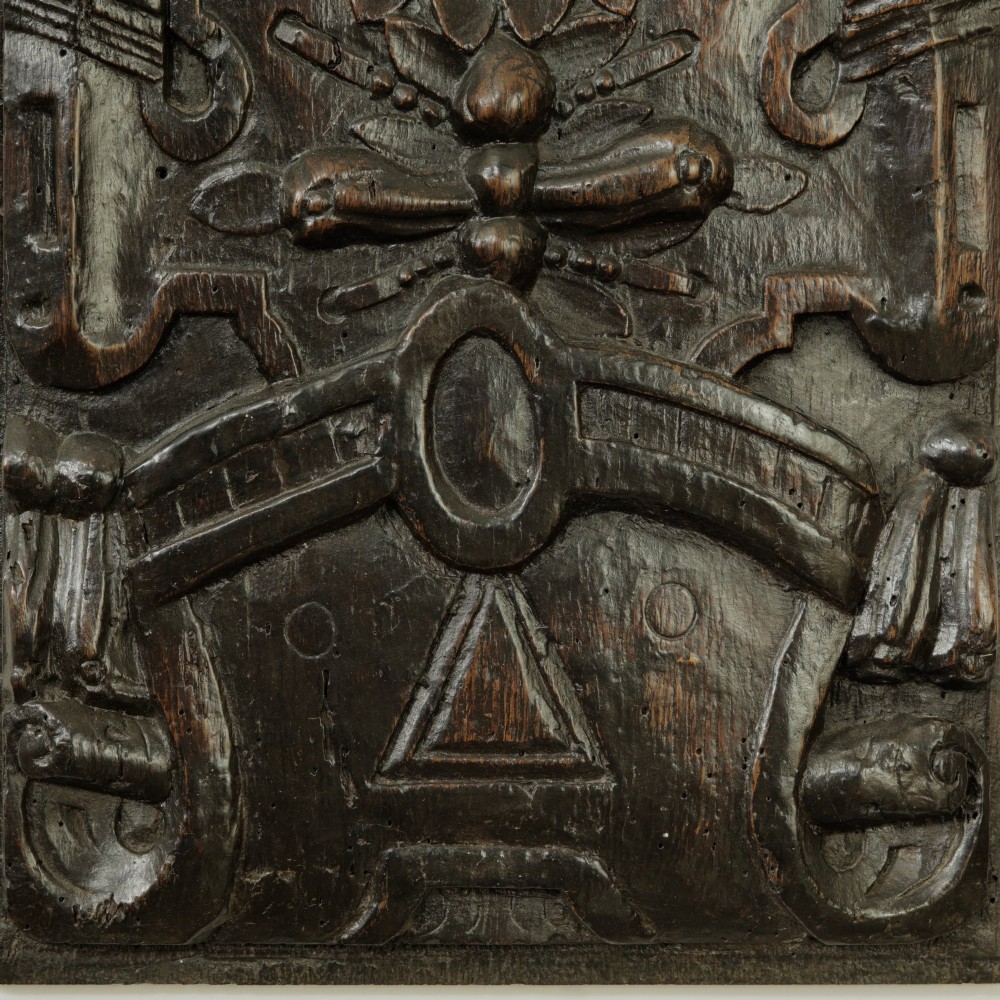 A rectangular dark oak timber panel featuring a high-relief hand carving of a winged cherub head surrounded by intricate scrollwork and geometric strapwork. View IV