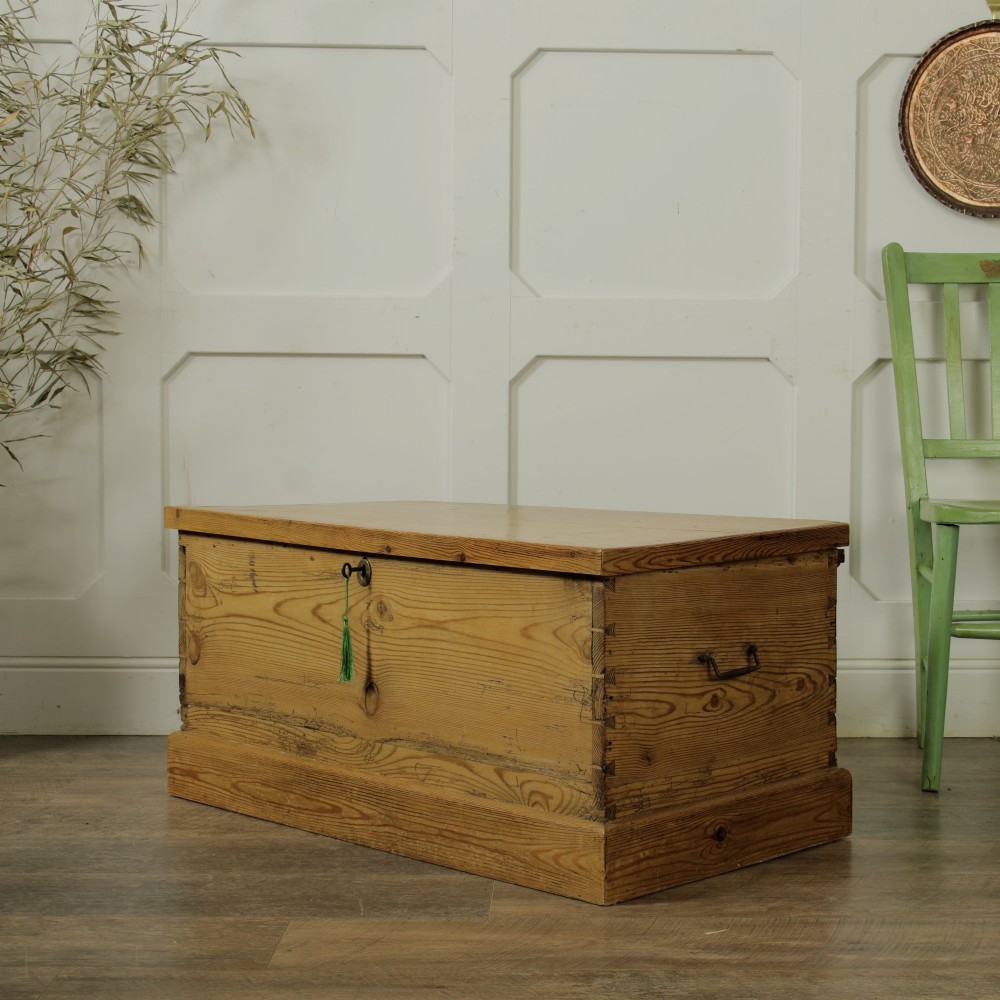 A rectangular Victorian pitch pine storage trunk featuring visible dovetail joinery, an iron keyhole escutcheon, metal side handles, and a plinth base.