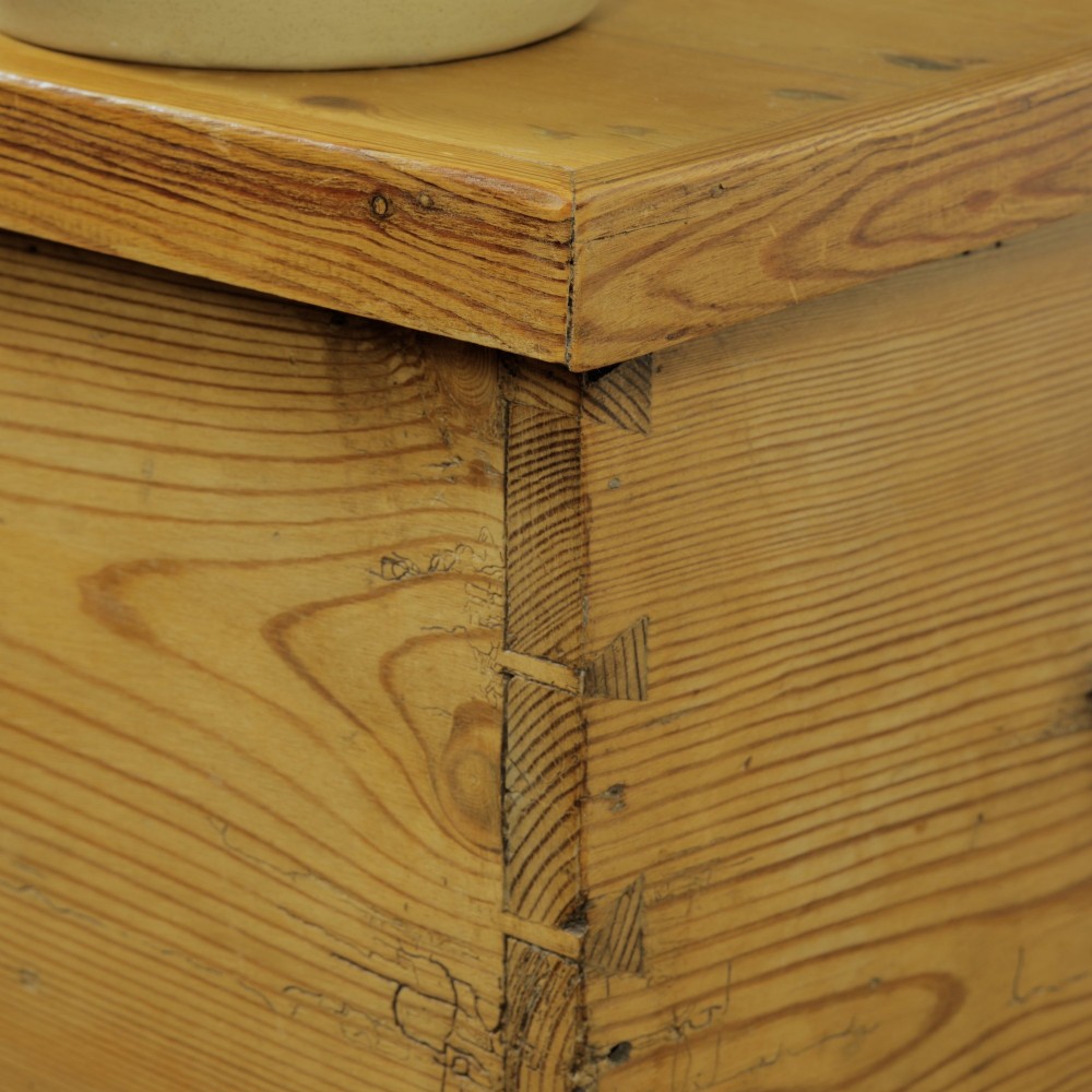 A rectangular Victorian pitch pine storage trunk featuring visible dovetail joinery, an iron keyhole escutcheon, metal side handles, and a plinth base. View VI