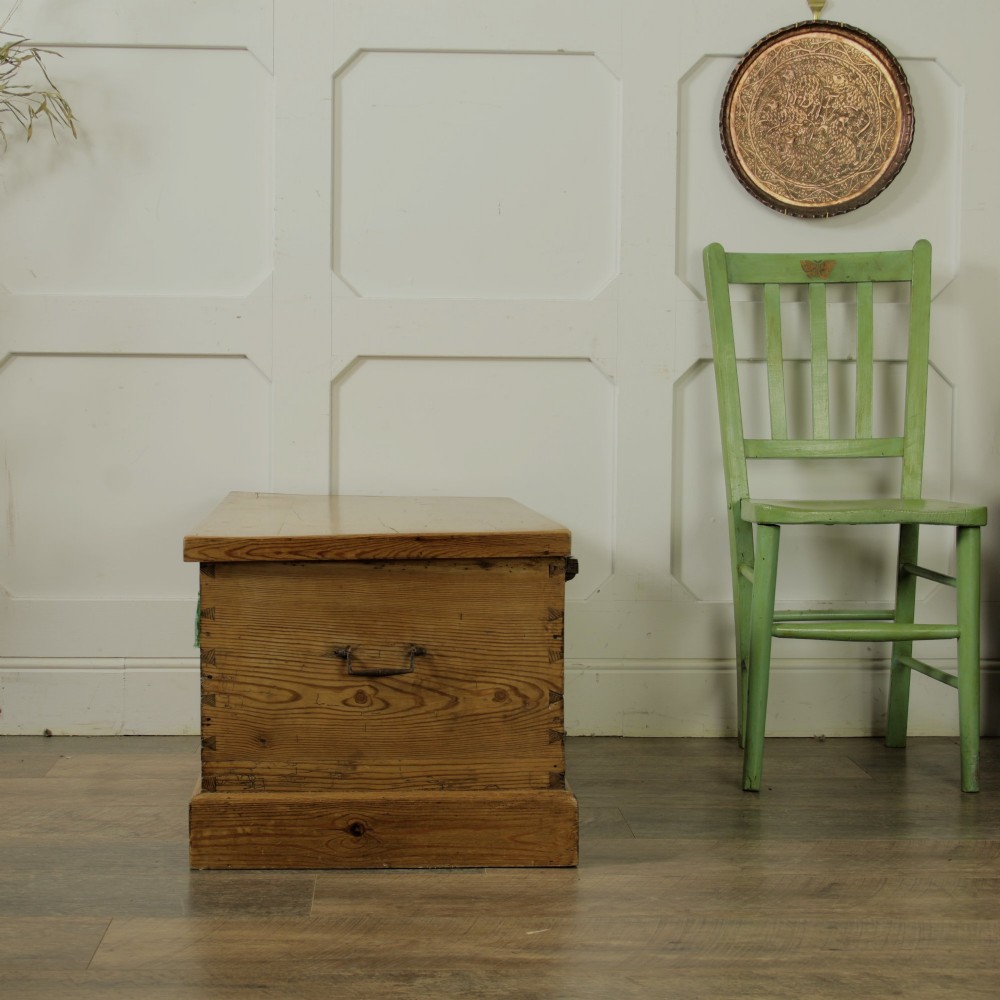 A rectangular Victorian pitch pine storage trunk featuring visible dovetail joinery, an iron keyhole escutcheon, metal side handles, and a plinth base. View XV