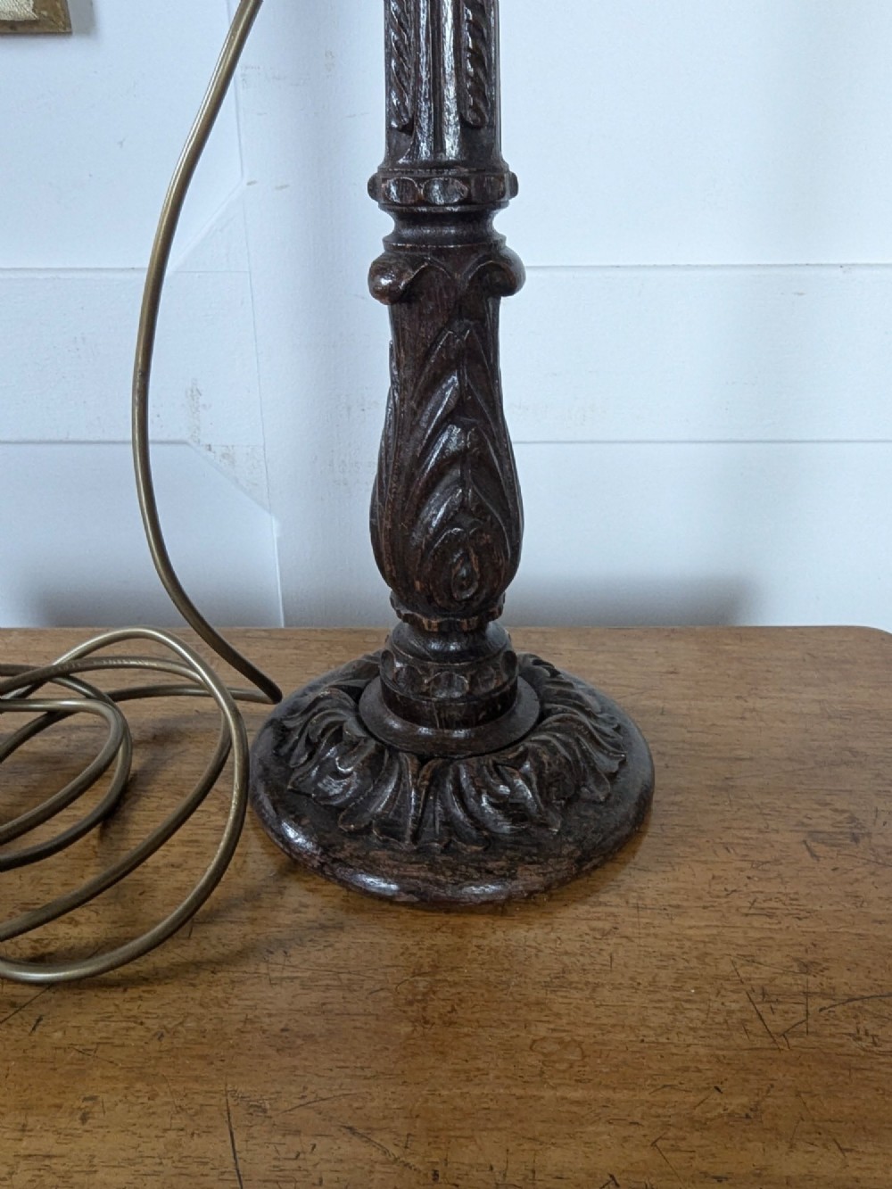A late Victorian carved dark oak candlestick table lamp base featuring detailed acanthus leaf carvings and an exposed filament bulb. View IV