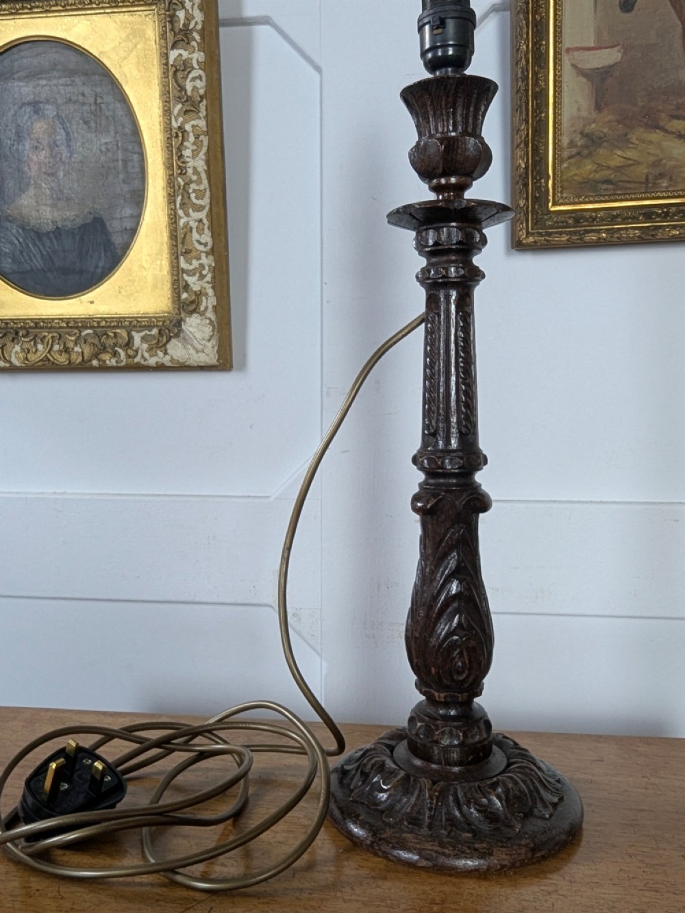 A late Victorian carved dark oak candlestick table lamp base featuring detailed acanthus leaf carvings and an exposed filament bulb. View V
