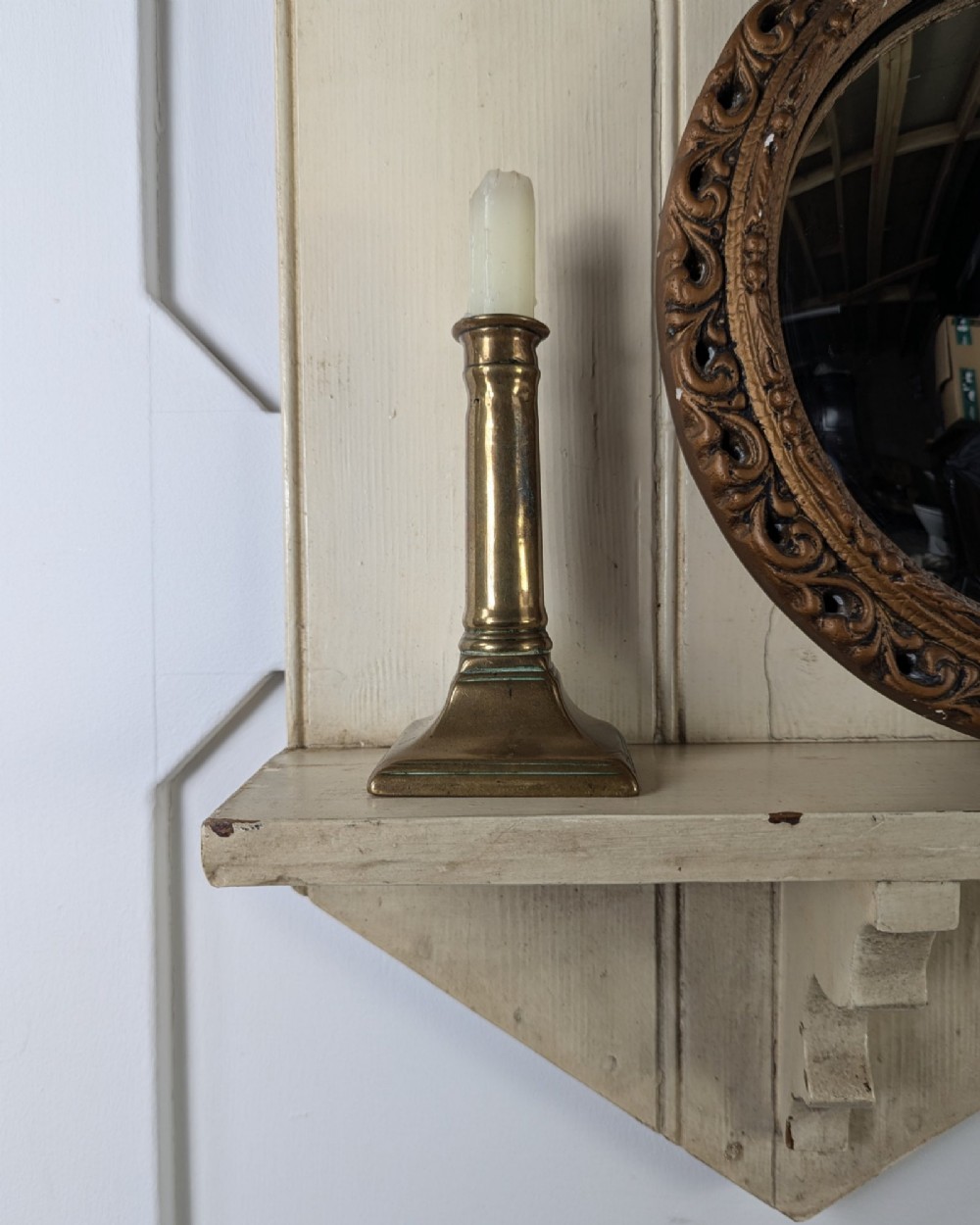 A brass candlestick featuring a square stepped base, a vertical cylindrical column stem, and a flared sconce holding a wax taper. View V