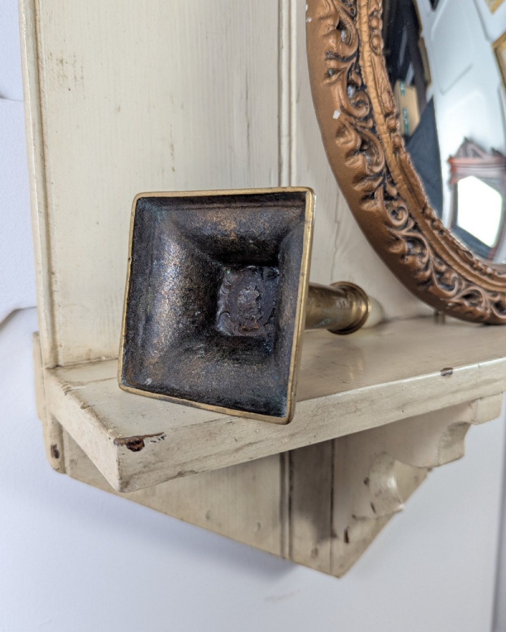 A brass candlestick featuring a square stepped base, a vertical cylindrical column stem, and a flared sconce holding a wax taper. View VI