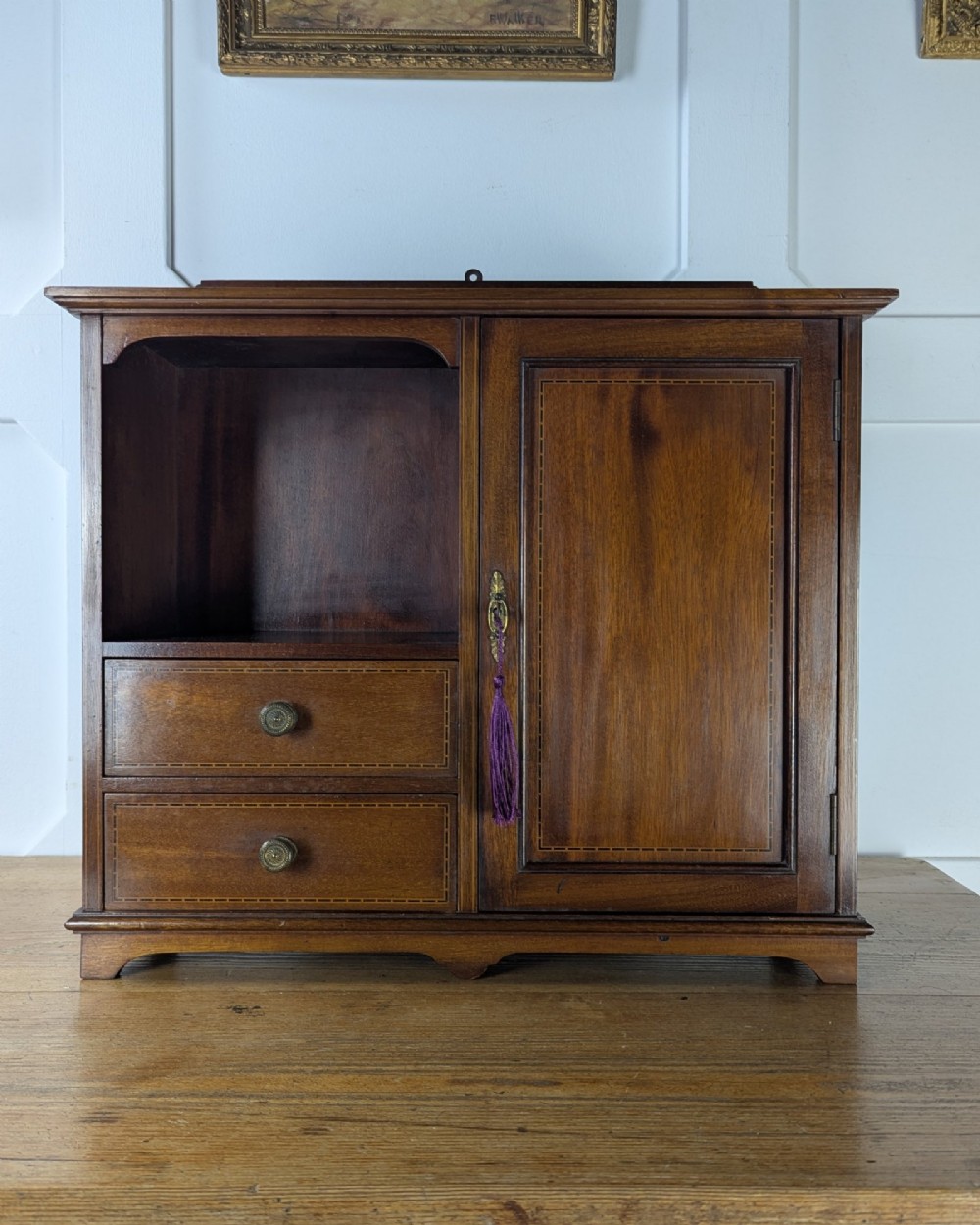 A late nineteenth-century warm brown wooden smokers cabinet featuring an open shelf over two drawers on the left, a single inlaid door on the right, and brass hardware.