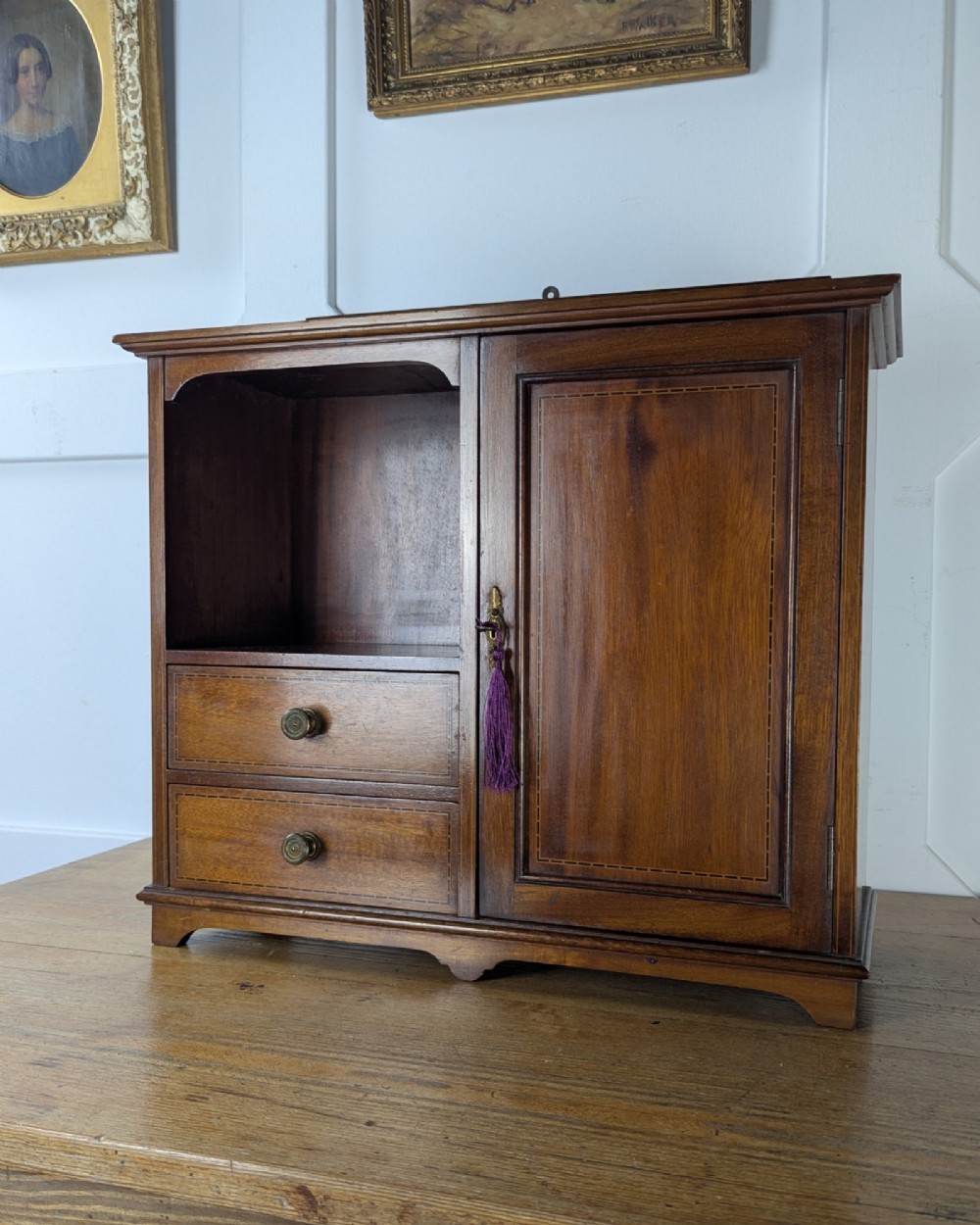 A late nineteenth-century warm brown wooden smokers cabinet featuring an open shelf over two drawers on the left, a single inlaid door on the right, and brass hardware. View II