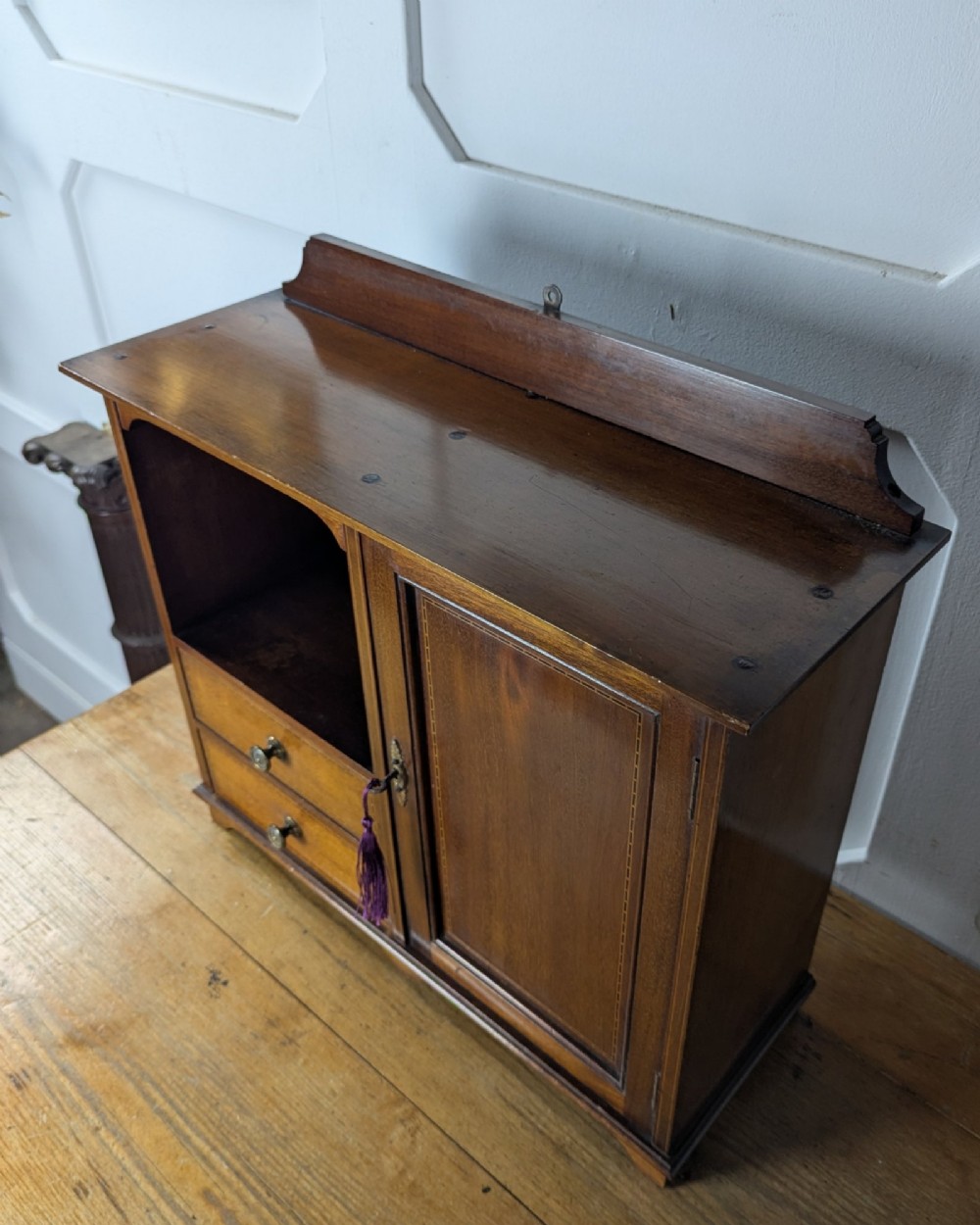 A late nineteenth-century warm brown wooden smokers cabinet featuring an open shelf over two drawers on the left, a single inlaid door on the right, and brass hardware. View VII