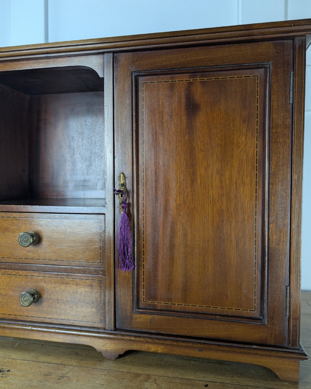 A late nineteenth-century warm brown wooden smokers cabinet featuring an open shelf over two drawers on the left, a single inlaid door on the right, and brass hardware. View XII