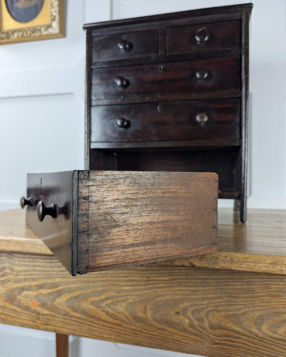 A 19th-century miniature wooden chest of drawers with a dark stained finish, two small top drawers over three long drawers, turned knobs, and brass escutcheons. View X