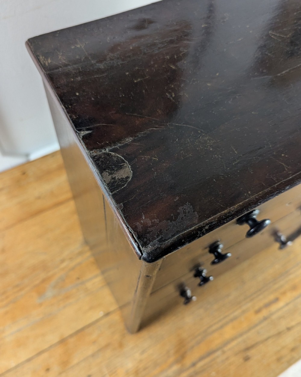 A 19th-century miniature wooden chest of drawers with a dark stained finish, two small top drawers over three long drawers, turned knobs, and brass escutcheons. View XIII
