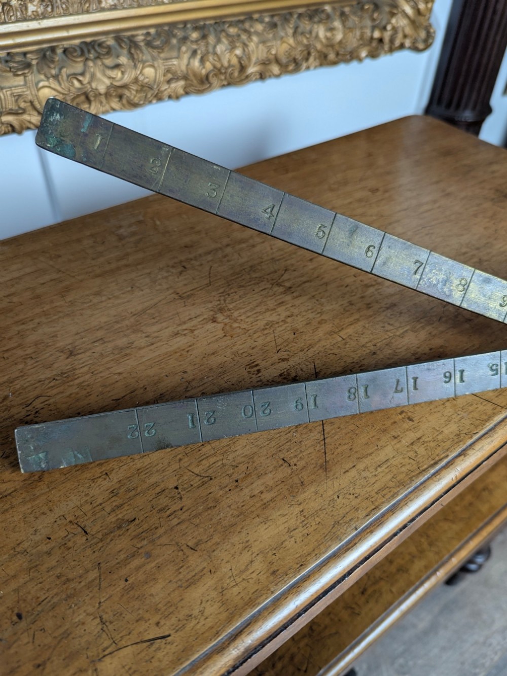 A solid brass folding ruler featuring stamped block text reading WINDSOR BURIAL BOARD resting on a wooden surface. View VII