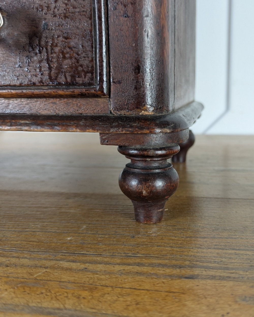 A dark brown Victorian miniature wooden chest of drawers with glass knobs and small turned feet. View VIII