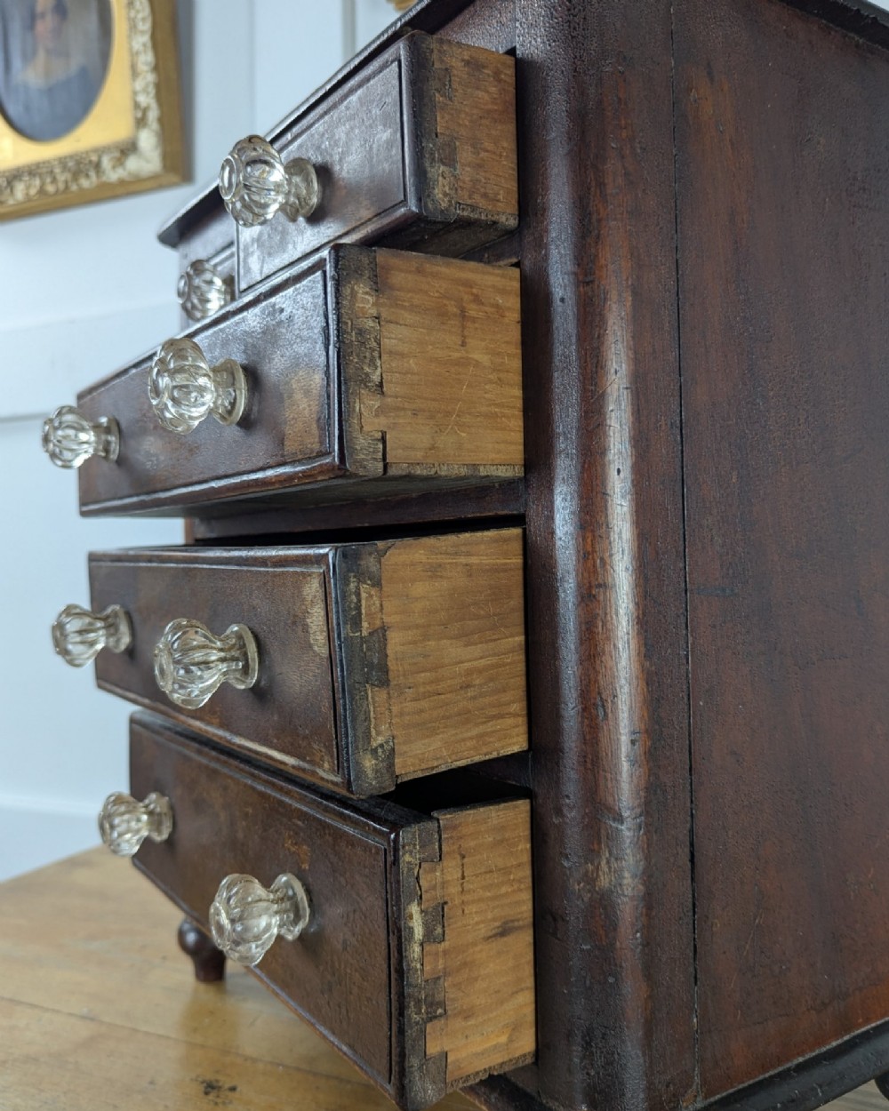 A dark brown Victorian miniature wooden chest of drawers with glass knobs and small turned feet. View IX