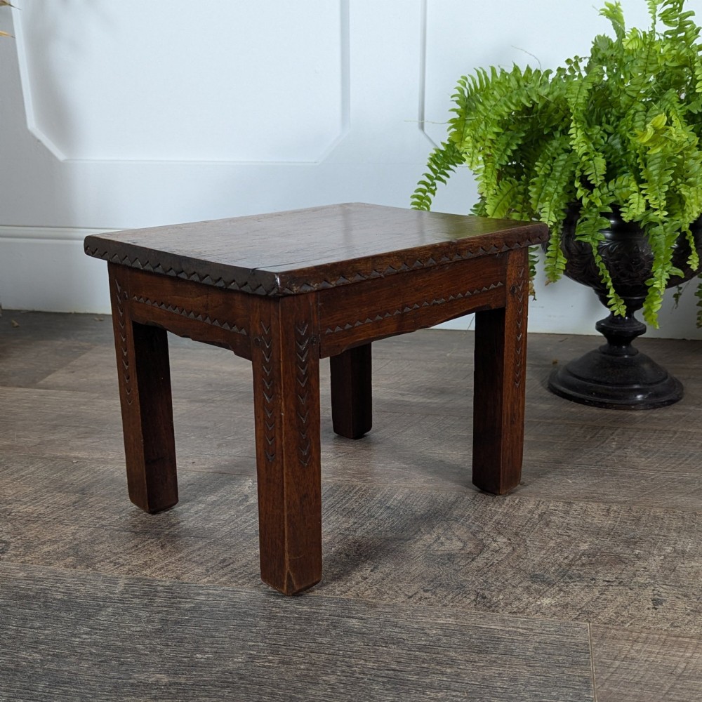 A rectangular dark oak low stool featuring hand-carved notch decorations along the apron and straight legs. View V