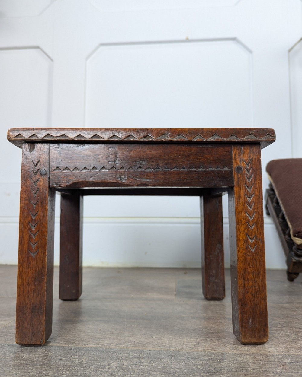 A rectangular dark oak low stool featuring hand-carved notch decorations along the apron and straight legs. View VII