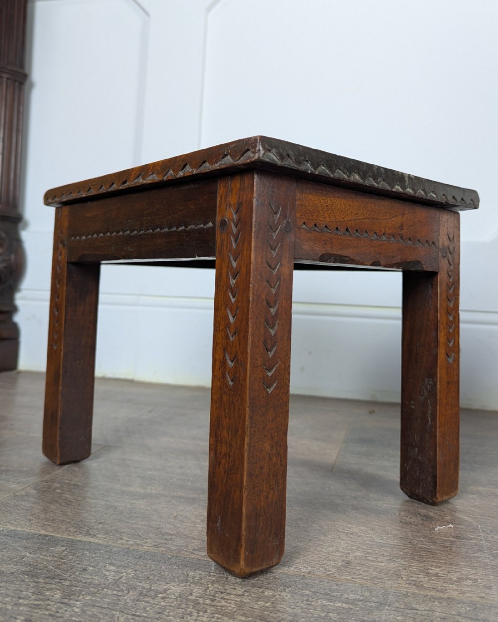 A rectangular dark oak low stool featuring hand-carved notch decorations along the apron and straight legs. View VIII