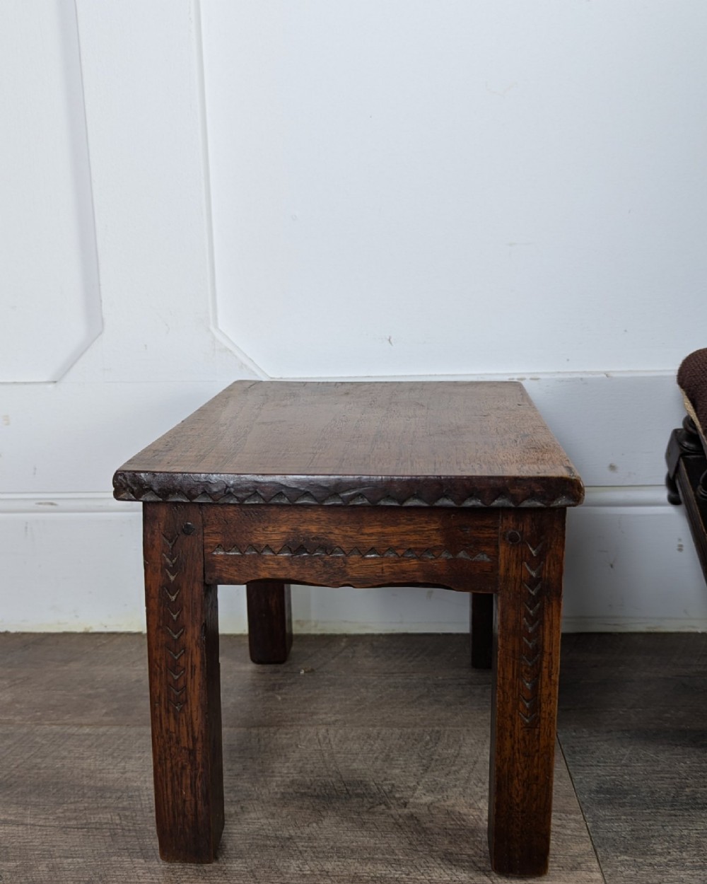 A rectangular dark oak low stool featuring hand-carved notch decorations along the apron and straight legs. View XI