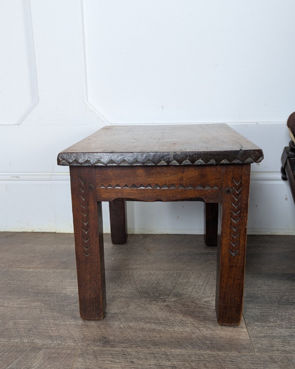 A rectangular dark oak low stool featuring hand-carved notch decorations along the apron and straight legs. View XII