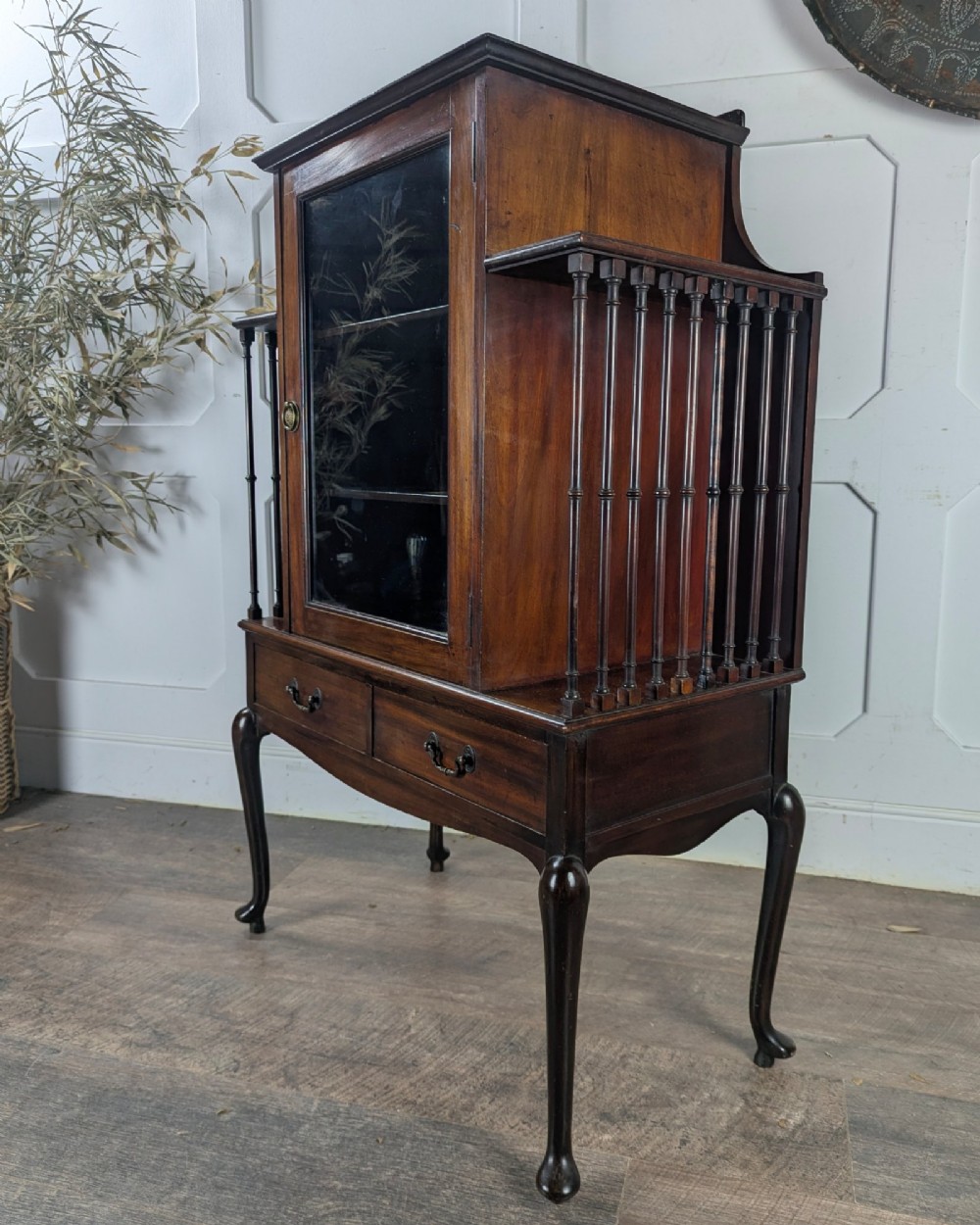 An early 20th-century mahogany music cabinet featuring a central glazed door flanked by turned spindle galleries, set above two drawers on cabriole legs. View IX