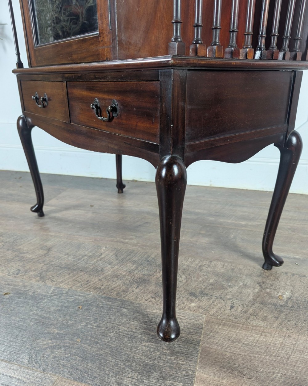 An early 20th-century mahogany music cabinet featuring a central glazed door flanked by turned spindle galleries, set above two drawers on cabriole legs. View X