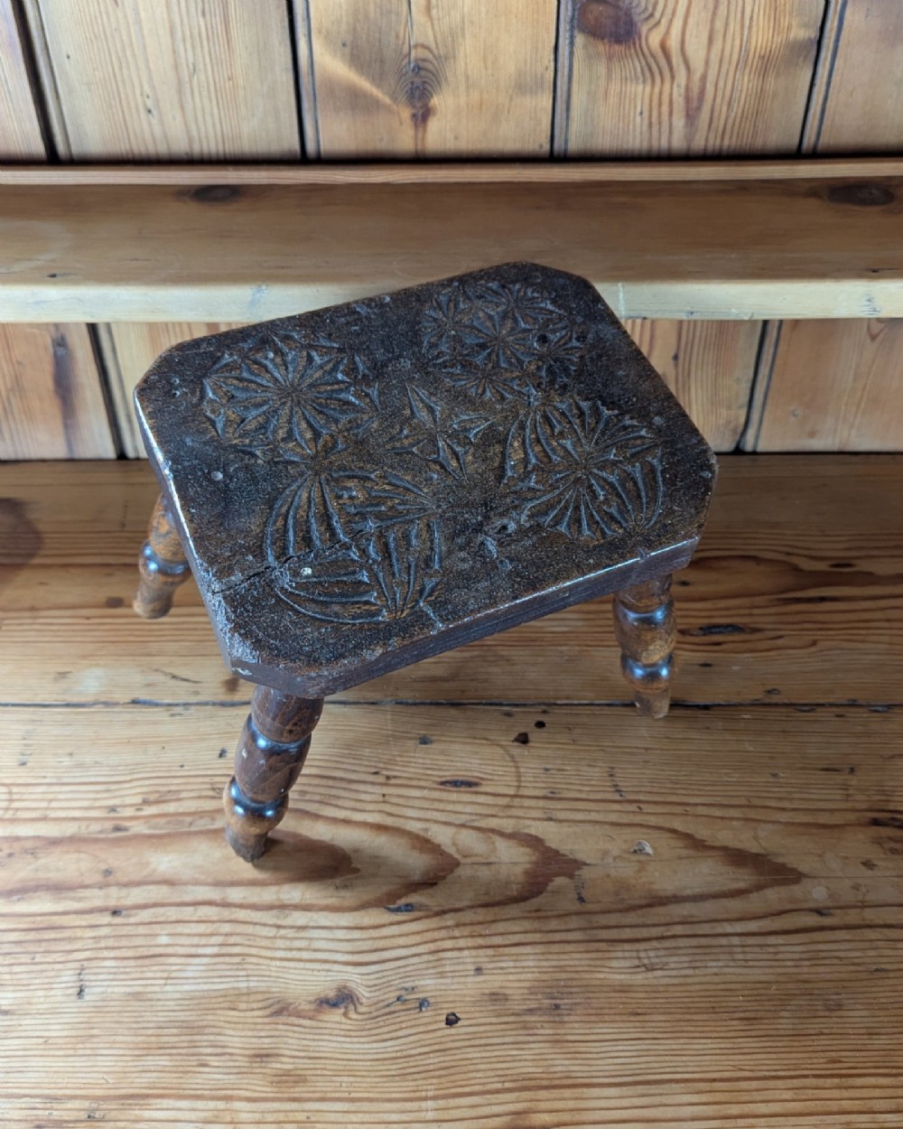 A dark oak 19th-century rectangular wooden stool featuring hand-carved rosette motifs on the seat top and four turned legs. View II