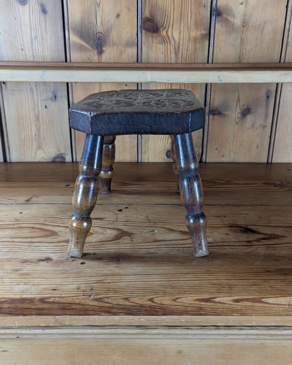 A dark oak 19th-century rectangular wooden stool featuring hand-carved rosette motifs on the seat top and four turned legs. View IV