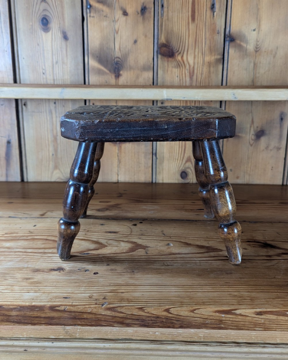 A dark oak 19th-century rectangular wooden stool featuring hand-carved rosette motifs on the seat top and four turned legs. View V